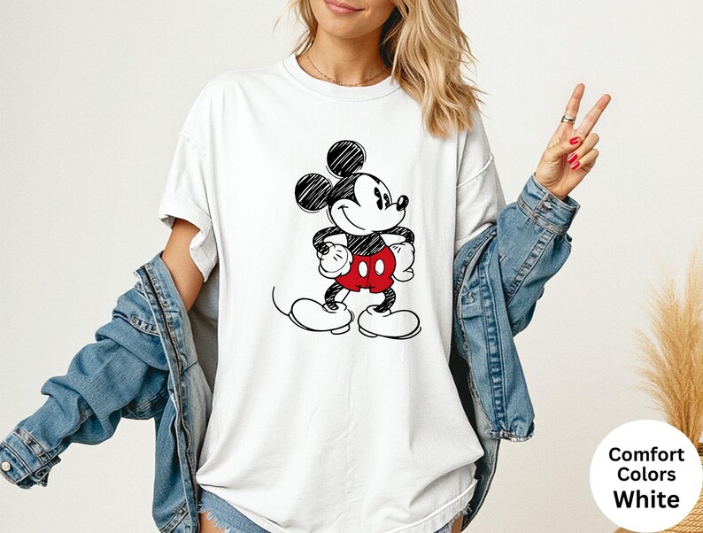 May include: White t-shirt featuring a black and red Mickey Mouse graphic. The cartoon character is drawn in a sketch style. The shirt is part of the Comfort Colors collection.