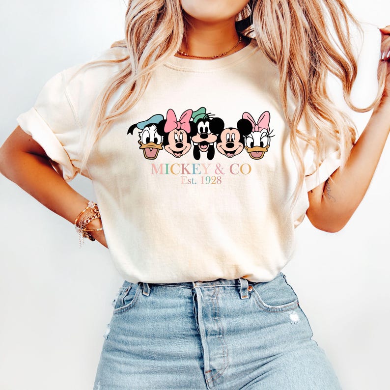 May include: A white t-shirt with a colorful graphic of Mickey Mouse, Minnie Mouse, Donald Duck, Goofy, and Pluto. The text "MICKEY & CO Est. 1928" is printed below the graphic.