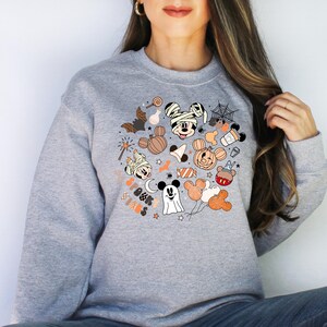 May include: Gray sweatshirt with a colorful graphic print of Mickey Mouse and friends dressed in Halloween costumes. The graphic includes candy, pumpkins, and ghosts. The text "Spooky Minis" is included in the graphic.