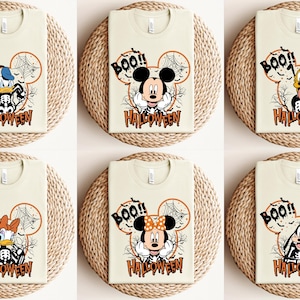 Puede incluir: Seis camisetas beige con un tema de Halloween con Mickey Mouse, Minnie Mouse, Donald Duck y Goofy. Cada camiseta tiene un personaje de dibujos animados con un disfraz de esqueleto y el texto "BOO!! HALLOWEEN".