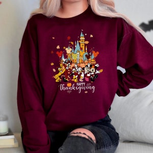 May include: A maroon sweatshirt with a graphic of Mickey Mouse and friends in front of a cartoon version of the Disney castle. The text "Happy Thanksgiving" is printed below the image.