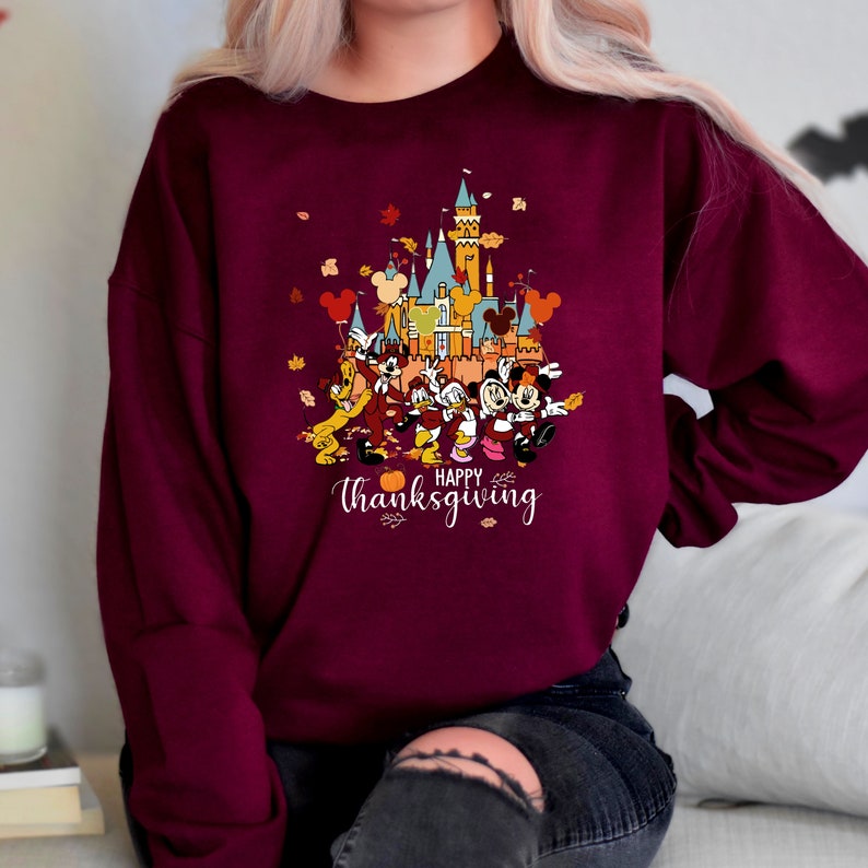 May include: A maroon sweatshirt with a graphic of Mickey Mouse and friends in front of a cartoon version of the Disney castle. The text "Happy Thanksgiving" is printed below the image.