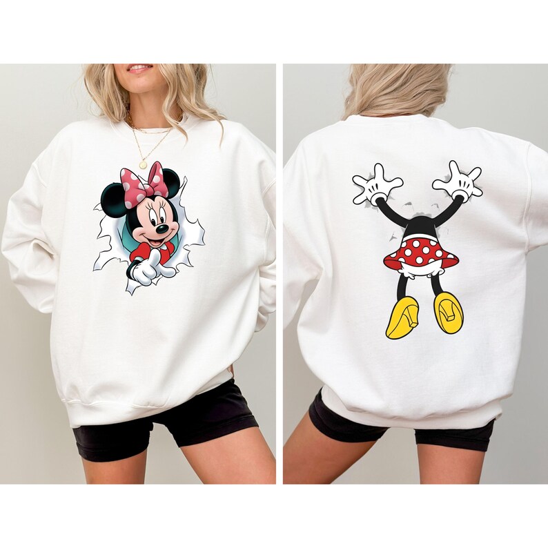 K&ouml;nnte beinhalten: Wei&szlig;es Sweatshirt mit einem Minnie Mouse-Design auf der Vorder- und R&uuml;ckseite. Die Vorderseite zeigt Minnie Mouse, die aus einem zerrissenen Effekt auftaucht, und die R&uuml;ckseite zeigt ihr Outfit. Das Design beinhaltet Rot, Schwarz, Wei&szlig; und Gelb.