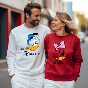 May include: A couple wearing matching sweatshirts. One sweatshirt is white with a Donald Duck graphic and the text "Her Donald". The other is red with a Daisy Duck graphic and the text "His Daisy".