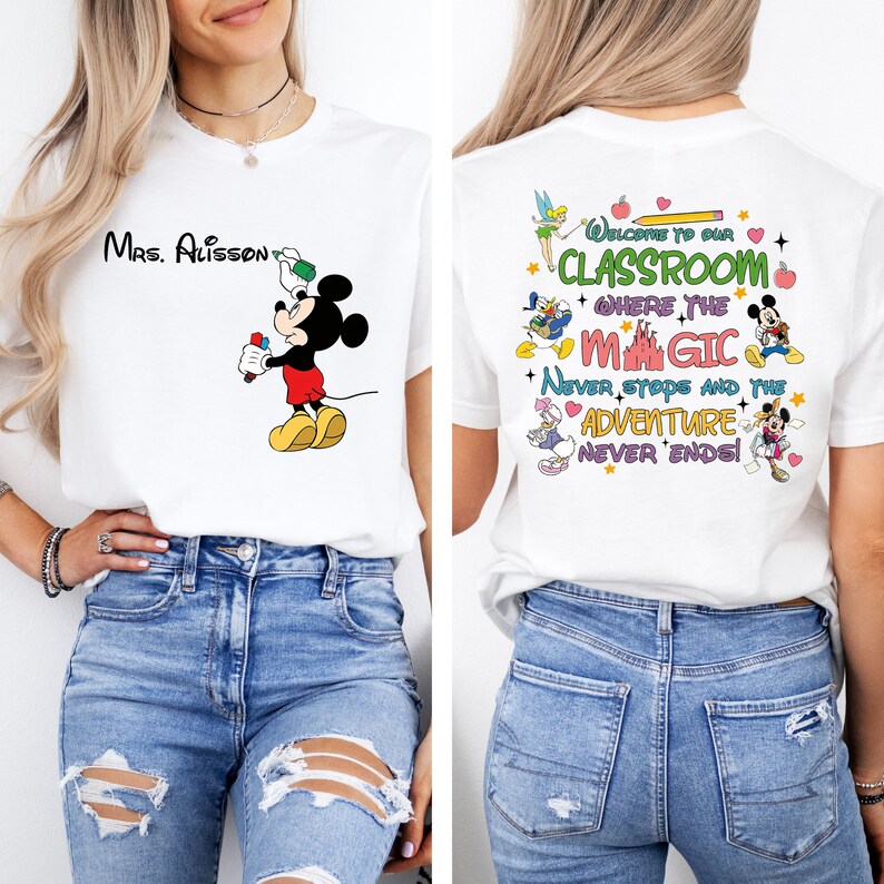 Puede incluir: Camiseta blanca con una ilustraci&oacute;n de Mickey Mouse sosteniendo un l&aacute;piz. La parte posterior de la camiseta tiene un dise&ntilde;o colorido con el texto "Bienvenido a nuestra aula donde la magia nunca se detiene y la aventura nunca termina!"