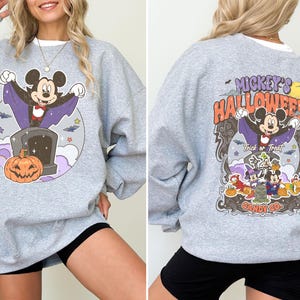 May include: Grey sweatshirt with a Mickey Mouse Halloween graphic. The graphic features Mickey Mouse dressed as a vampire with a pumpkin and the text "Mickey's Halloween Candy Co."