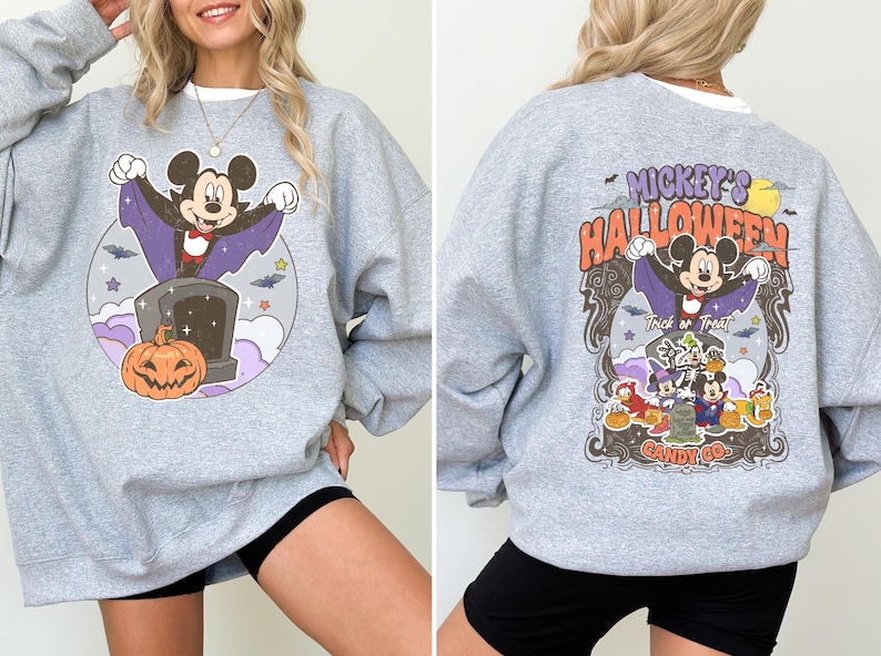 May include: Grey sweatshirt with a Mickey Mouse Halloween graphic. The graphic features Mickey Mouse dressed as a vampire with a pumpkin and the text "Mickey's Halloween Candy Co."