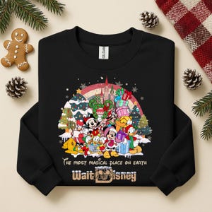 Op de afbeelding: Zwarte crewneck sweatshirt met een kleurrijke afbeelding van Disney-personages, kerstbomen en een regenboog. De tekst "The most magical place on earth" en "Walt Disney" staan eronder gedrukt.