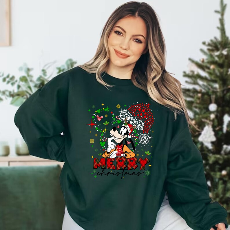 May include: Green Christmas sweatshirt with a cartoon image of Goofy wearing a Santa hat and surrounded by red and green Christmas lights. The text "Merry Christmas" is printed below Goofy.