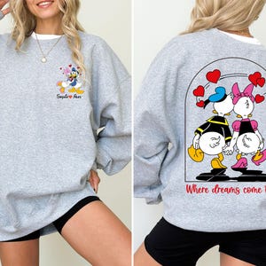 May include: Gray sweatshirt with a cartoon image of Donald and Daisy Duck holding hands in a heart-shaped archway with the text "Where dreams come true". The front of the sweatshirt has a smaller image of Donald and Daisy Duck with the text "Sequoia + Alex".
