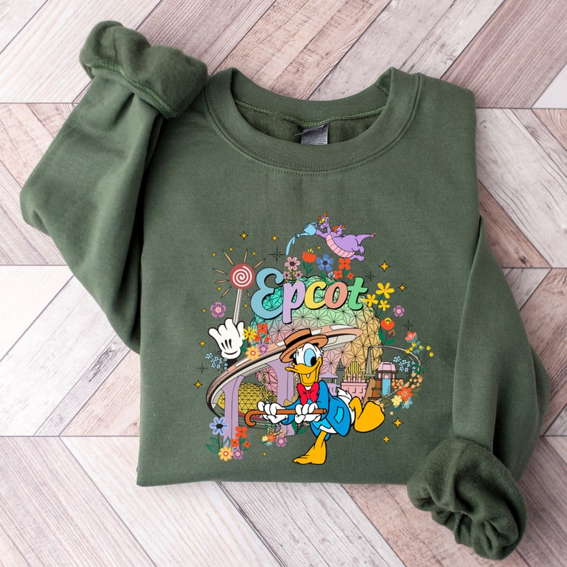 May include: A green sweatshirt with a colorful graphic of Donald Duck in front of the Epcot logo. The graphic also includes a dragon, flowers, and a lollipop.