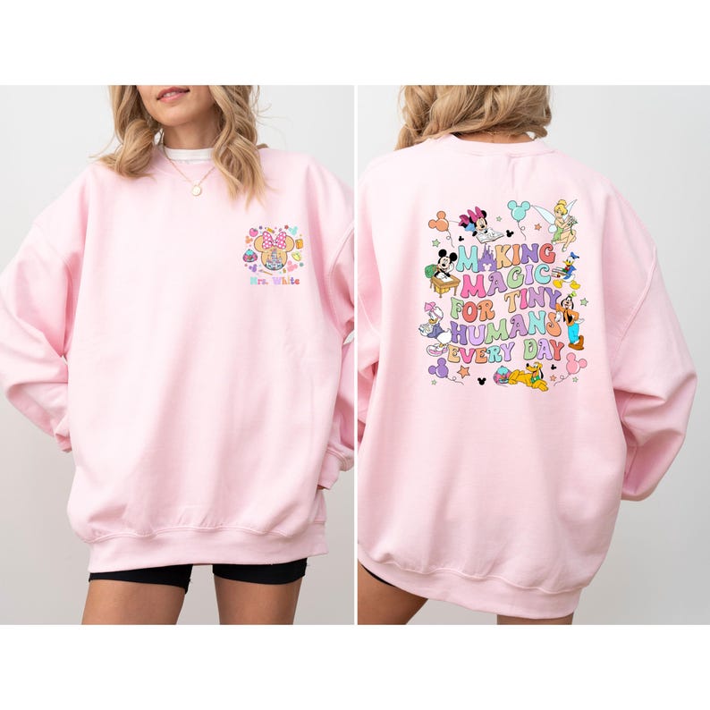 May include: A light pink sweatshirt with a Minnie Mouse graphic on the front and a colorful Disney-themed design on the back. The back design includes the text "MAKING MAGIC FOR TINY HUMANS EVERY DAY".