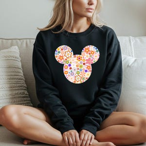 May include: Black sweatshirt featuring a floral Mickey Mouse design. The design is composed of various colorful flowers in shades of orange, pink, yellow, and blue. The sweatshirt is a crew neck style.