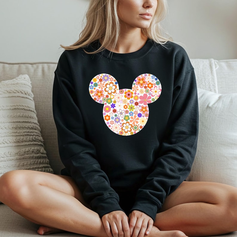 May include: Black sweatshirt featuring a floral Mickey Mouse design. The design is composed of various colorful flowers in shades of orange, pink, yellow, and blue. The sweatshirt is a crew neck style.