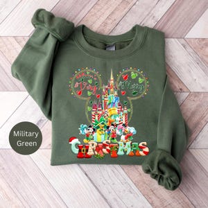 May include: A green sweatshirt with a Mickey Mouse Christmas design. The design features Mickey Mouse's ears with the words "A Very Merry Christmas" inside. The centre of the design features Mickey Mouse and friends in front of Cinderella's Castle.