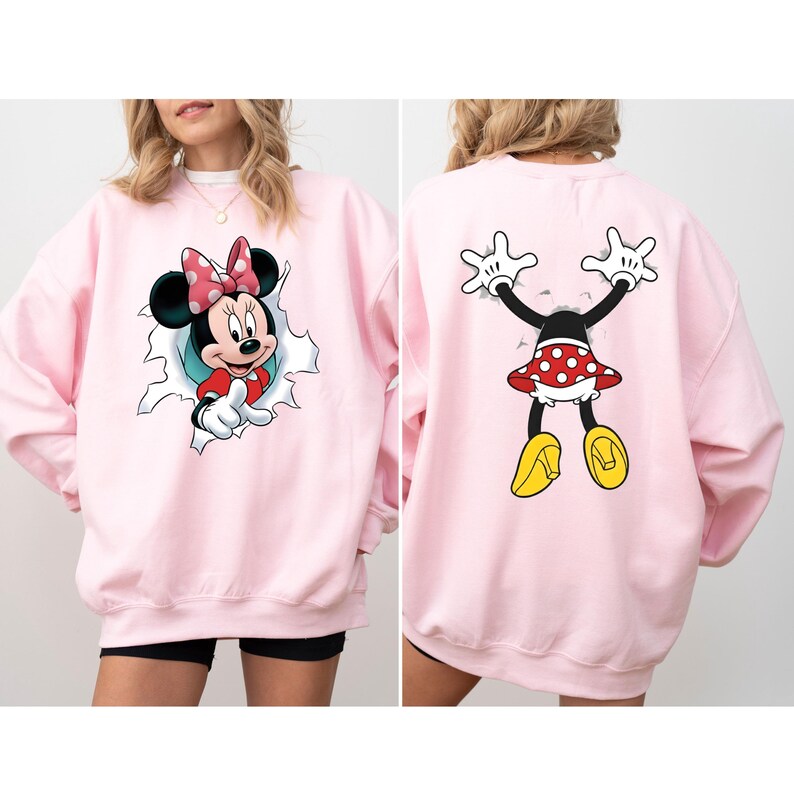 K&ouml;nnte beinhalten: Ein hellrosa Sweatshirt mit einem Minnie Mouse-Motiv. Auf der Vorderseite ist Minnie, die aus einem Loch kommt, und auf der R&uuml;ckseite ist sie von hinten zu sehen. Minnie tr&auml;gt einen rot-wei&szlig; gepunkteten Rock und eine Schleife.
