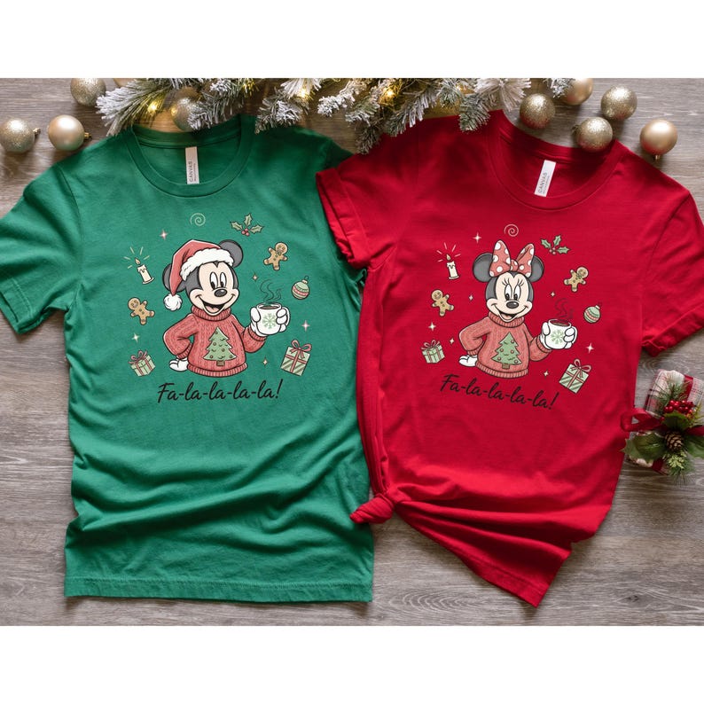 May include: Two Christmas-themed t-shirts, one green and one red. Each shirt features a cartoon character wearing a holiday sweater and holding a mug. The text "Fa-la-la-la-la!" is printed below the character. Festive and fun.