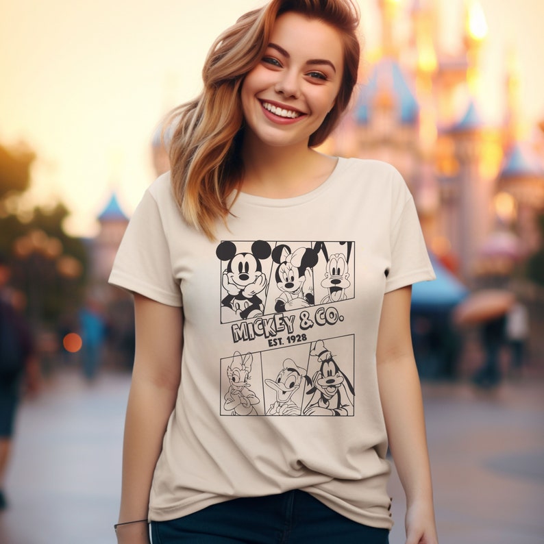 K&ouml;nnte beinhalten: Ein beiges T-Shirt mit einem schwarz-wei&szlig;en Grafikdruck von Mickey Mouse, Minnie Mouse, Goofy, Donald Duck und Pluto. Die Grafik enth&auml;lt den Text "Mickey & Co. Est. 1928".