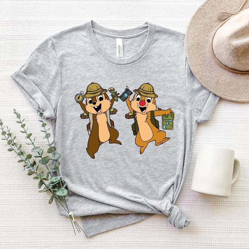 May include: Grey t-shirt featuring a graphic of two cartoon chipmunks wearing explorer hats and carrying backpacks. The chipmunks are holding a compass, a camera, and a map.