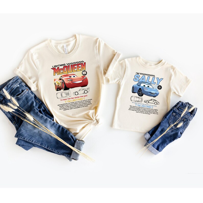 May include: Two cream-colored t-shirts featuring Lightning McQueen and Sally from the Cars movie. The Lightning McQueen shirt has a red car graphic and the text "Lightning McQueen 95". The Sally shirt has a blue car graphic and the name "Sally".