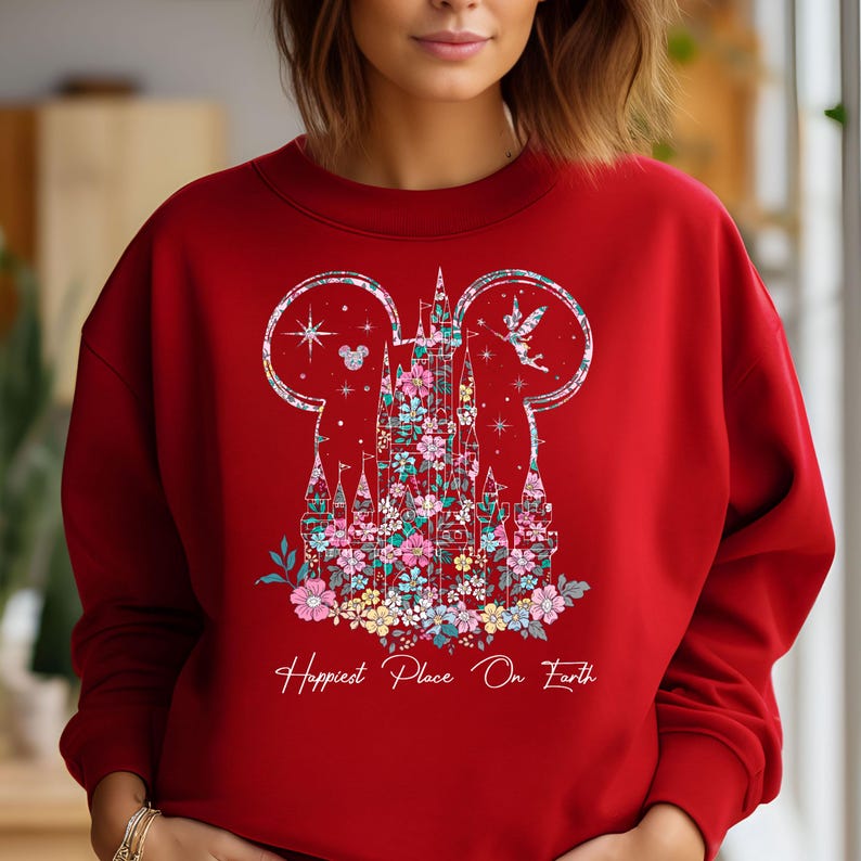 May include: Red sweatshirt with a floral design of Cinderella's castle in the shape of Mickey Mouse ears. The text "Happiest Place On Earth" is printed below the design.
