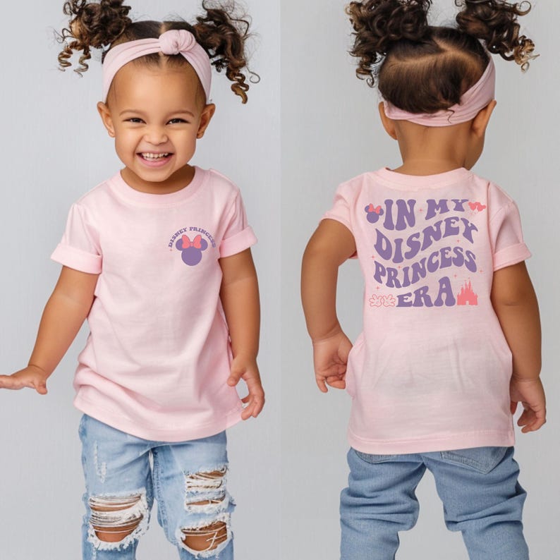 Puede incluir: Una camiseta rosa de manga corta con una cabeza de Mickey Mouse morada con un lazo rosa en la parte delantera y el texto "Disney Princess Era" en morado en la parte posterior. La camiseta la lleva puesta un ni&ntilde;o.