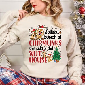 May include: A white long-sleeved shirt with a Christmas-themed design featuring Chipmunks from Disney's 'Chip 'n Dale Rescue Rangers'. The text reads "Jolliest bunch of Chipmunks this side of the Nut House".