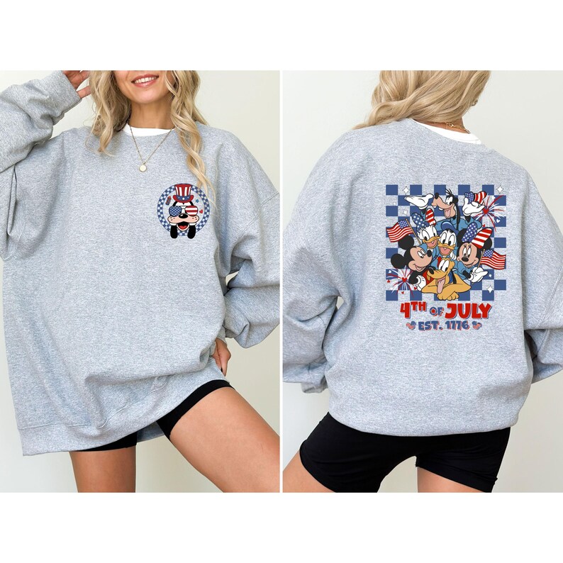 Puede incluir: Una sudadera gris con un dise&ntilde;o patri&oacute;tico. La parte delantera tiene un gr&aacute;fico circular con un personaje de dibujos animados en un cami&oacute;n. La parte trasera muestra un patr&oacute;n de cuadros con personajes de dibujos animados y el texto "4th of July Est. 1776".