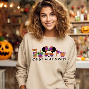 May include: A tan sweatshirt with a graphic of Mickey Mouse and friends dressed in Halloween costumes. The text "BEST DAY EVER" is printed below the graphic.