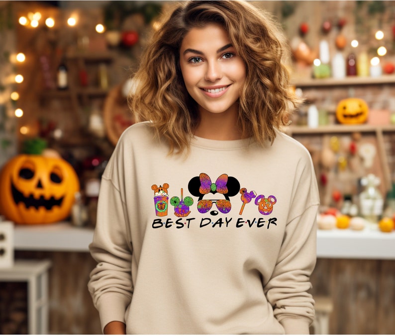May include: A tan sweatshirt with a graphic of Mickey Mouse and friends dressed in Halloween costumes. The text "BEST DAY EVER" is printed below the graphic.