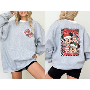 May include: A light gray sweatshirt with a white collar. The front features a candy cane design. The back has a graphic of Mickey and Minnie Mouse in Santa hats with the words "Merry Christmas".