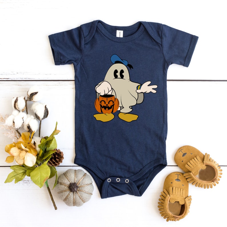 Puede incluir: Un body de beb&eacute; azul marino con un fantasma de dibujos animados que lleva un gorro de marinero azul y sostiene una calabaza de Halloween. El fantasma sonr&iacute;e y tiene ojos grandes.