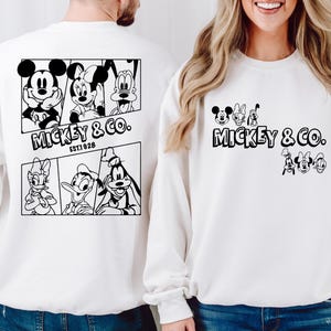 May include: Two white sweatshirts with black Mickey Mouse and friends graphics. The larger sweatshirt has a graphic of Mickey Mouse, Minnie Mouse, Donald Duck, and Goofy. The smaller sweatshirt has a graphic of Mickey Mouse, Minnie Mouse, Donald Duck, and Goofy. Both sweatshirts have the text "Mickey & Co. Est. 1928".