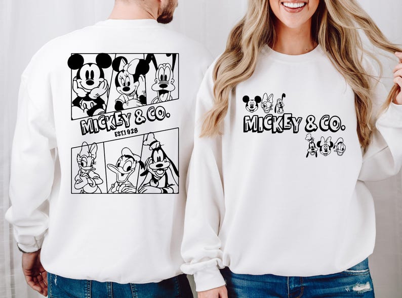 May include: Two white sweatshirts with black Mickey Mouse and friends graphics. The larger sweatshirt has a graphic of Mickey Mouse, Minnie Mouse, Donald Duck, and Goofy. The smaller sweatshirt has a graphic of Mickey Mouse, Minnie Mouse, Donald Duck, and Goofy. Both sweatshirts have the text "Mickey & Co. Est. 1928".