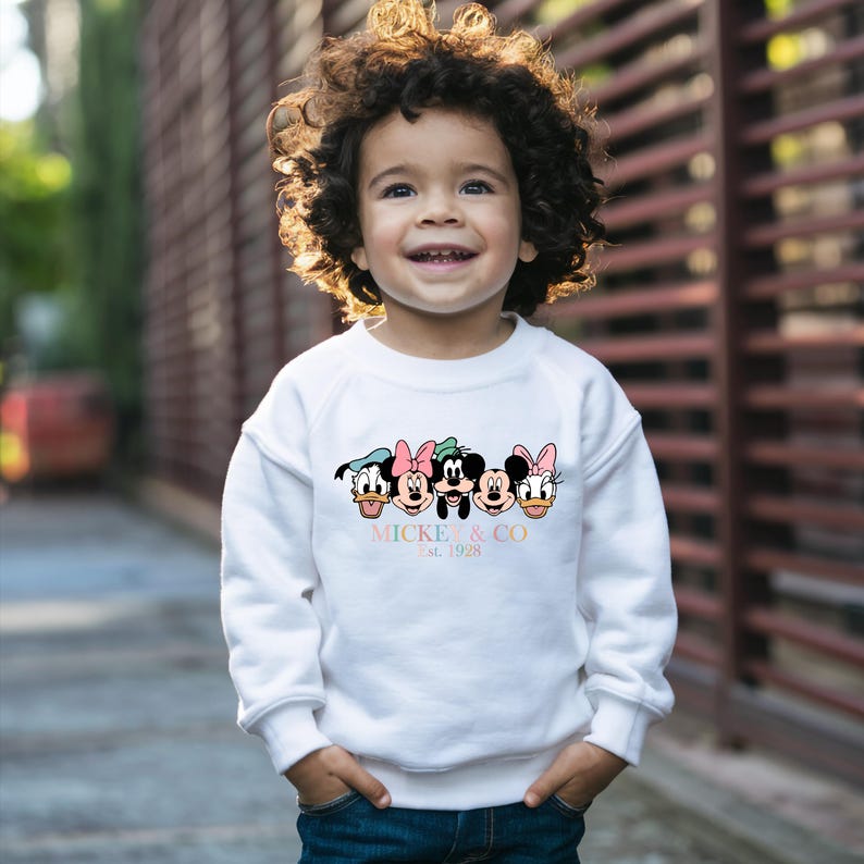 May include: White sweatshirt with a colorful graphic of Mickey Mouse and friends. The text "Mickey & Co. Est. 1928" is printed below the graphic.