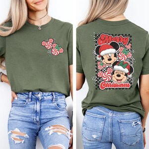 May include: Olive green t-shirt featuring a Christmas design. The front has a candy cane Mickey Mouse design. The back has Mickey and Minnie Mouse wearing Santa hats with the words "Merry Christmas" and "Christmas".