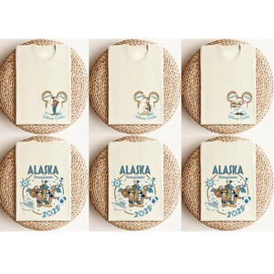 May include: Six cream-colored t-shirts with Disney Cruise graphics. The top row features Mickey Mouse ears with the text "Disney Cruise" and "2023". The bottom row displays "ALASKA" with Disney characters and the year "2025".