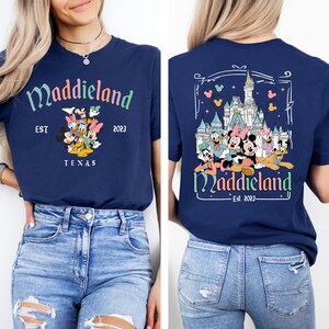 May include: A navy blue t-shirt with a graphic of Mickey Mouse and friends in front of Cinderella's Castle. The text "Maddieland Est. 2023" is printed on the shirt.