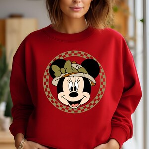 May include: Red sweatshirt with a graphic of Mickey Mouse wearing a safari hat. The graphic is surrounded by a checkered border.