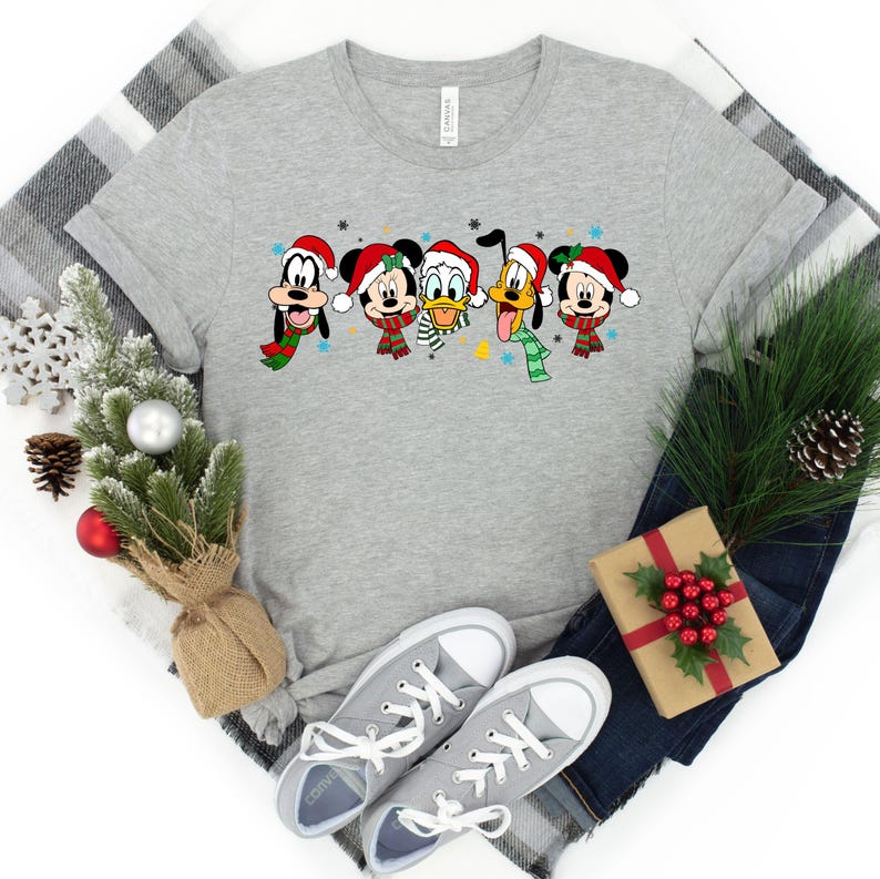 May include: A gray t-shirt with a Christmas-themed design featuring Mickey Mouse, Donald Duck, Goofy, and Pluto wearing Santa hats and scarves.