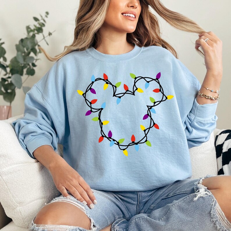 May include: Light blue sweatshirt with a graphic of a Mickey Mouse head made of colorful Christmas lights.
