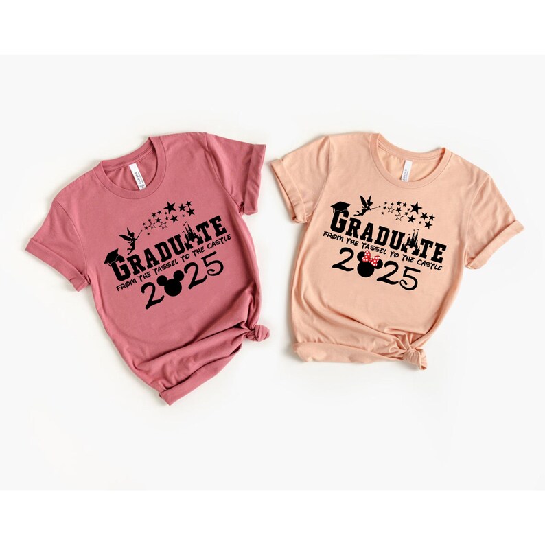 以下が含まれることがあります： 卒業をテーマにしたTシャツ2枚。Tシャツはピンクとピーチで、黒いグラフィックに「Graduate from the tassel to the castle 2025」の文字が書かれています。グラフィックには、ミッキーマウスの頭、城、星も含まれています。