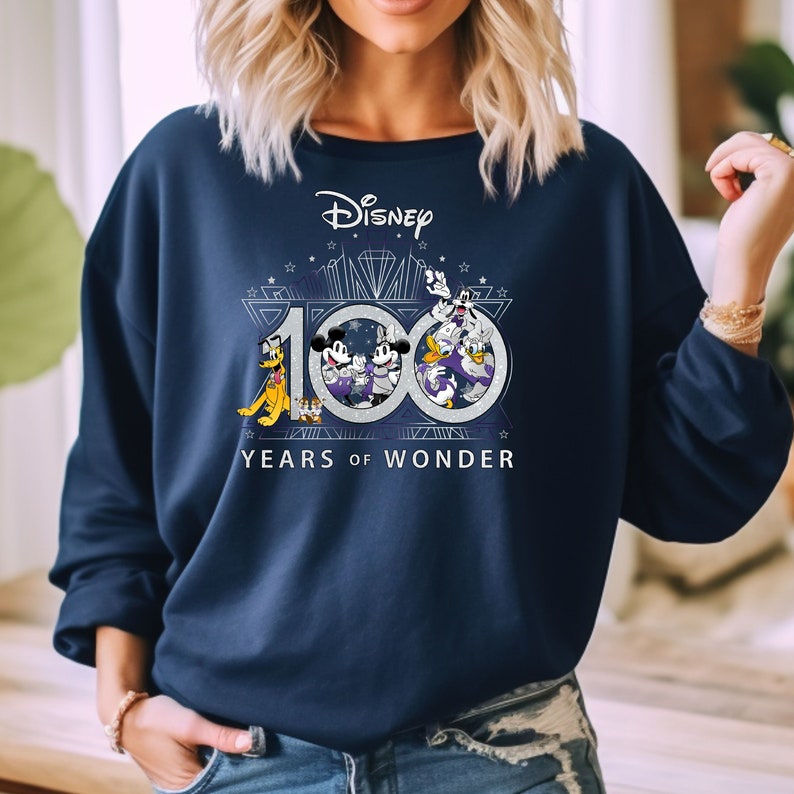 May include: A navy blue sweatshirt with a silver graphic of Mickey Mouse, Minnie Mouse, Donald Duck, Goofy, and Pluto celebrating Disney's 100th anniversary. The graphic includes the text "Disney" and "100 Years of Wonder".