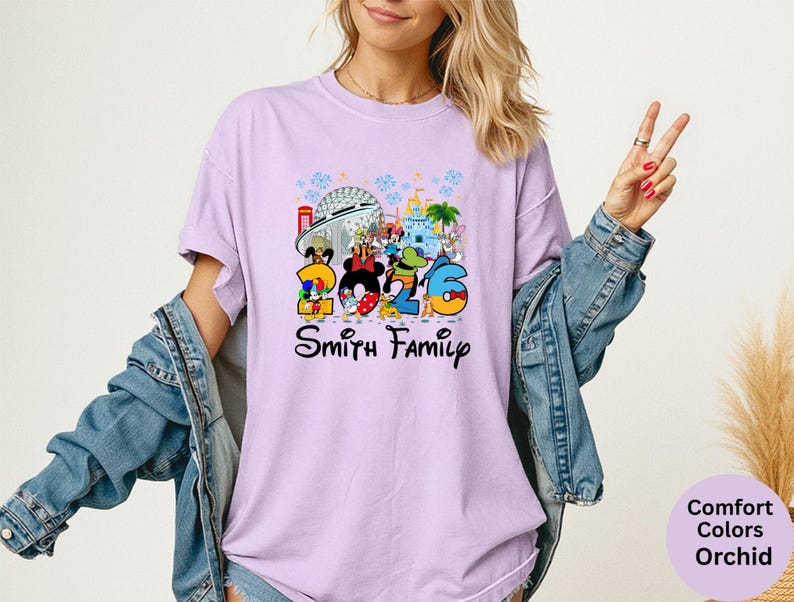 May include: A light purple t-shirt featuring a colorful graphic of Disney characters and the number "2026". The text "Smith Family" is below the graphic. The shirt is a Comfort Colors Orchid.