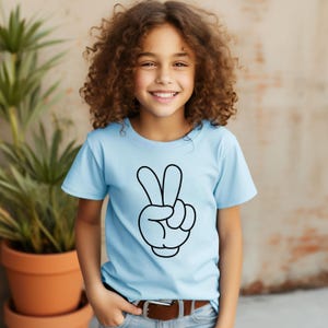 K&ouml;nnte beinhalten: Hellblaues T-Shirt mit einem schwarzen Cartoon-Hand-Friedenszeichen. Das kurz&auml;rmlige Oberteil hat einen Rundhalsausschnitt. Das Design ist mittig auf der Vorderseite des Shirts platziert.