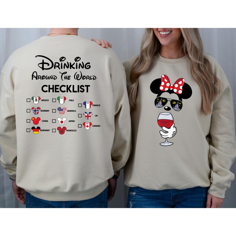Puede incluir: Una sudadera beige con el texto "Drinking Around the World Checklist" y una lista de pa&iacute;ses con banderas. La sudadera tiene una cabeza de Mickey Mouse con una copa de vino y gafas de sol.