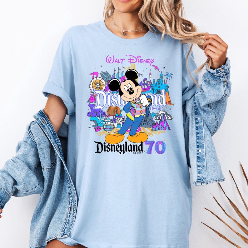May include: Light blue t-shirt with a colorful graphic of Mickey Mouse and Disneyland attractions. The text "Walt Disney" and "Disneyland Resort 70" is printed on the shirt.