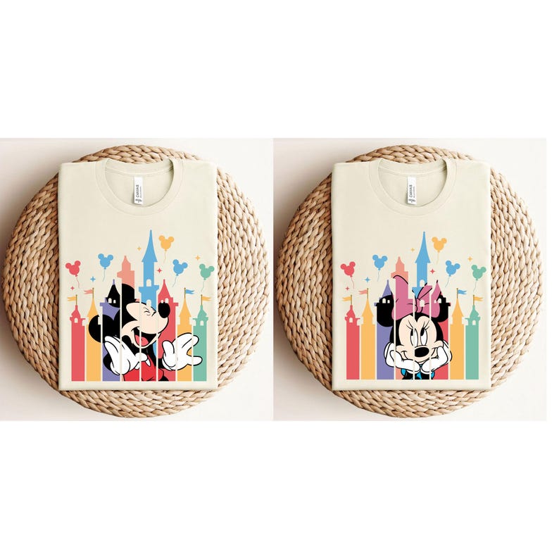 May include: Two cream colored t-shirts with a colorful castle silhouette and Mickey Mouse and Minnie Mouse cartoon characters. The castle silhouette has rainbow colored towers and pink, yellow, and blue balloons.