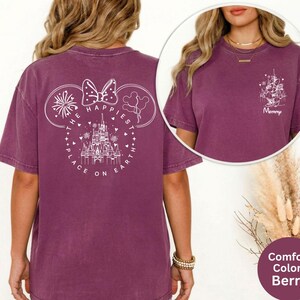 May include: Berry-colored t-shirt with a white graphic on the back featuring a castle, fireworks, and the text "The Happiest Place on Earth." A smaller graphic on the front says "Mommy." The shirt is a comfort color.