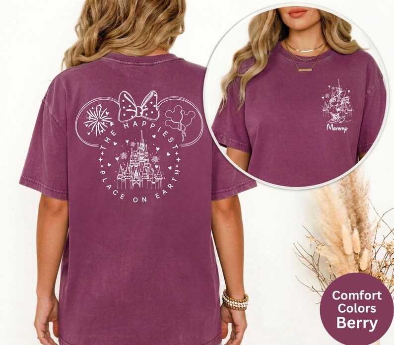 May include: Berry-colored t-shirt with a white graphic on the back featuring a castle, fireworks, and the text "The Happiest Place on Earth." A smaller graphic on the front says "Mommy." The shirt is a comfort color.